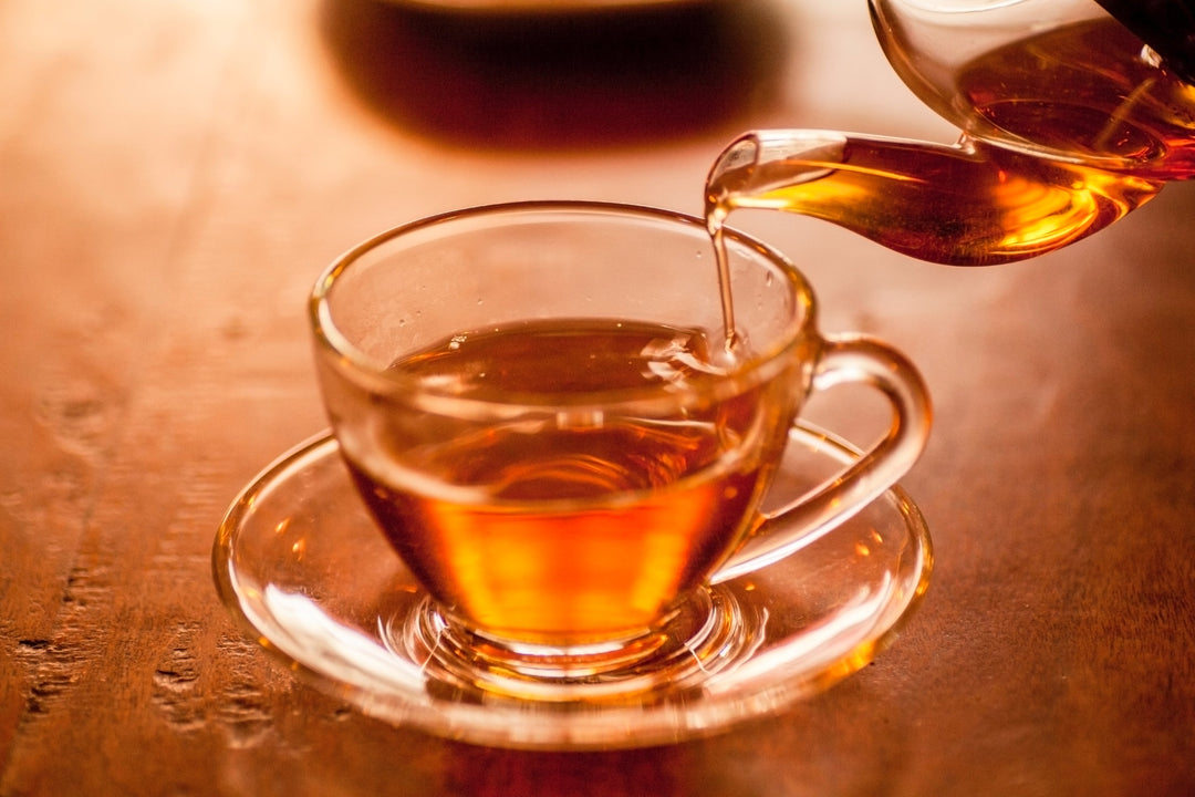 Tee wird aus einer Glas Teekanne in eine Glastasse gefüllt.