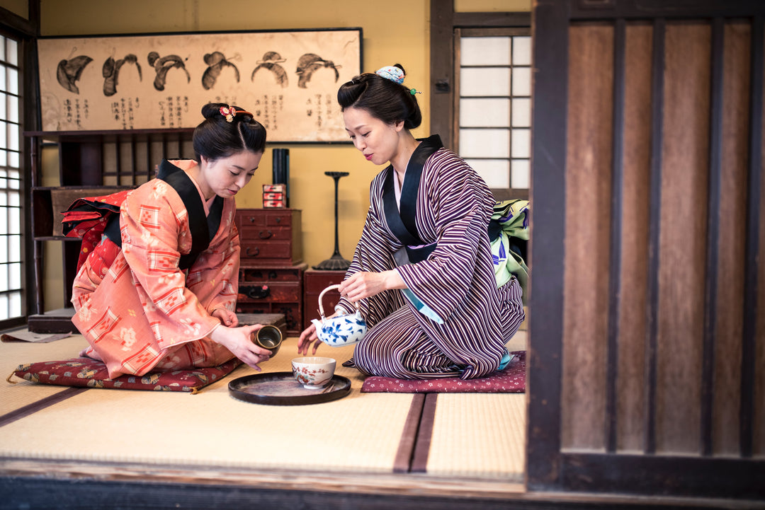 Zwei Japanerinnen, die einen Kimono tragen, trinken Tee drinnen, in der Teestube.