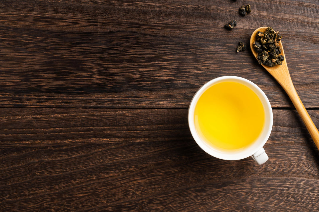 frischer Formosa Oolong auf Holzlöffel und aufgebrüht in einer Tasse (Tee hat schöne, gelbe Farbe)