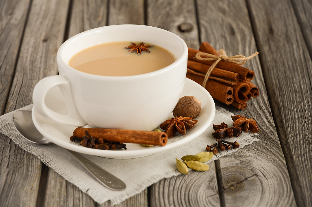 Chai Tee in einer weißen Teetasse, drumherum Zimtstangen