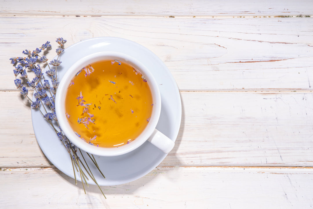 Kräutertee aufgebrüht in einer weißen Teetasse, zur Deko Lavendel daneben