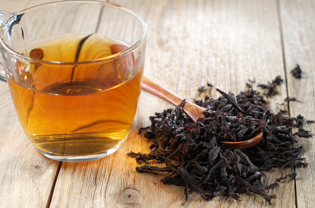Aufgebrühter Ceylon Tee mit Goldgelber Tassenfarbe im Glas, davor lose Teeblätter