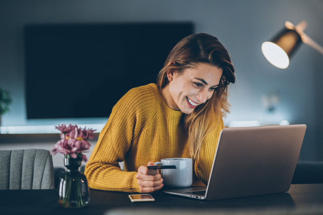 Frau mit Teetasse in der Hand schaut auf Laptop